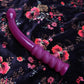 Wine colored dildo with curved body, bulbous head, and ergonomic handle at the base ribbed to hug your fingers. Toy laying on a floral sheet.