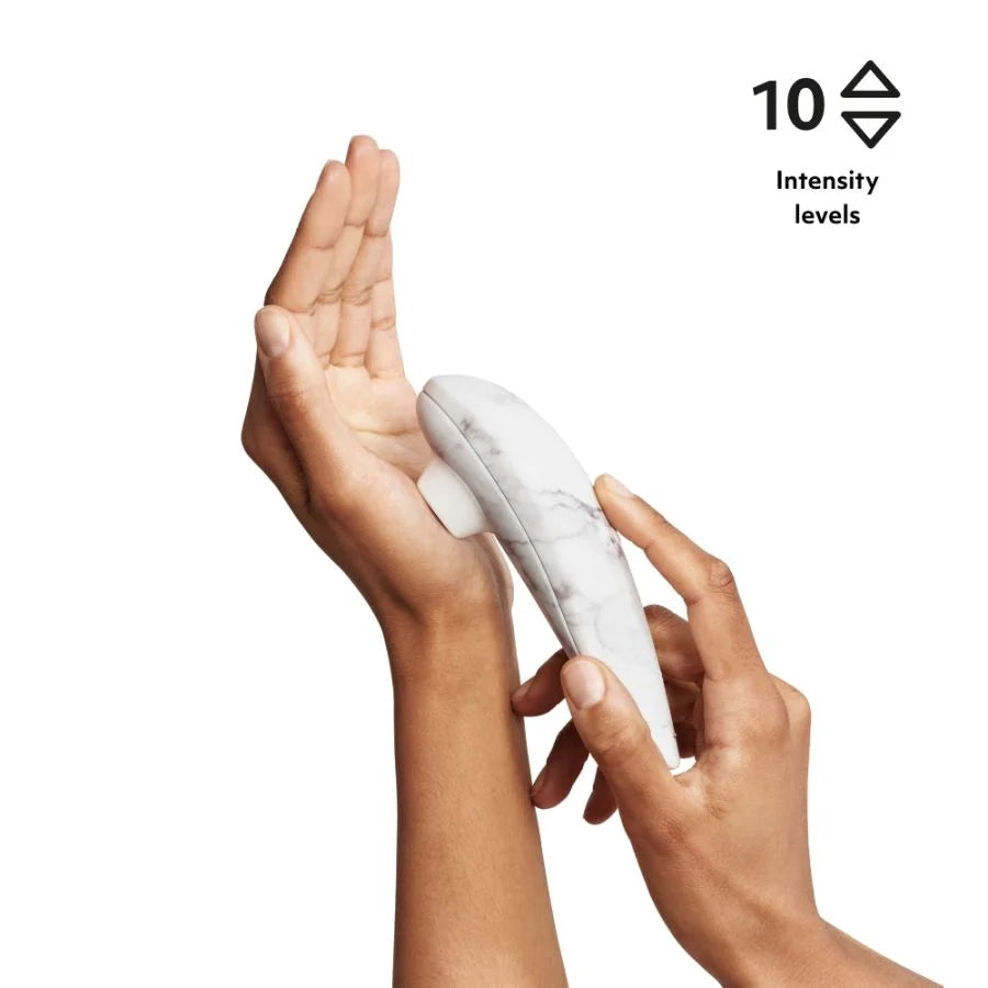 Someone holding a white marble clitoral stimulator with oval shaped opening running along the palm of their other hand. 10 intensity levels