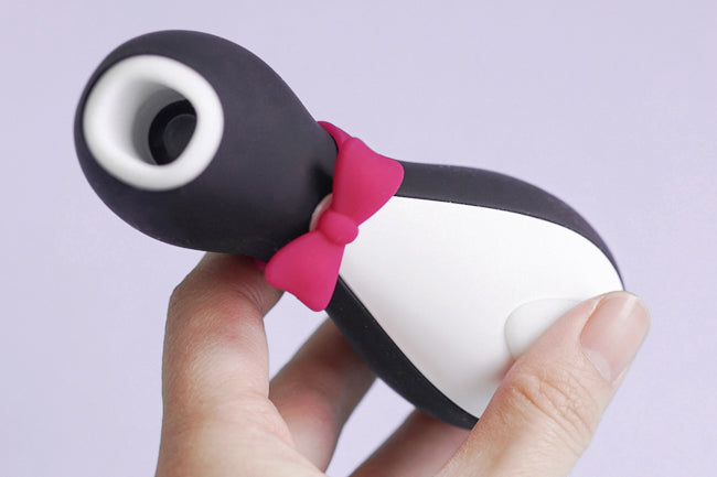 Penguin looking clitoral stimulator. Black and white design with open mouth at top and purple bowtie on the neck. Clitoral massager fits in palm of hand.