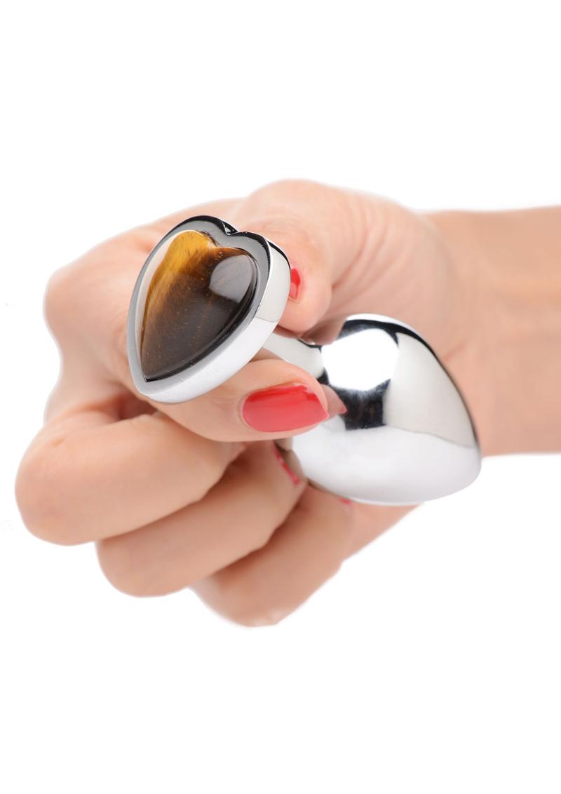 hand holding aluminum anal plug with bulbous teardrop shape. Base is heart shaped with tiger eye gem in center. 