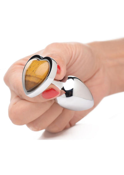 hand holding aluminum anal plug with bulbous teardrop shape. Base is heart shaped with tiger eye gem in center. 